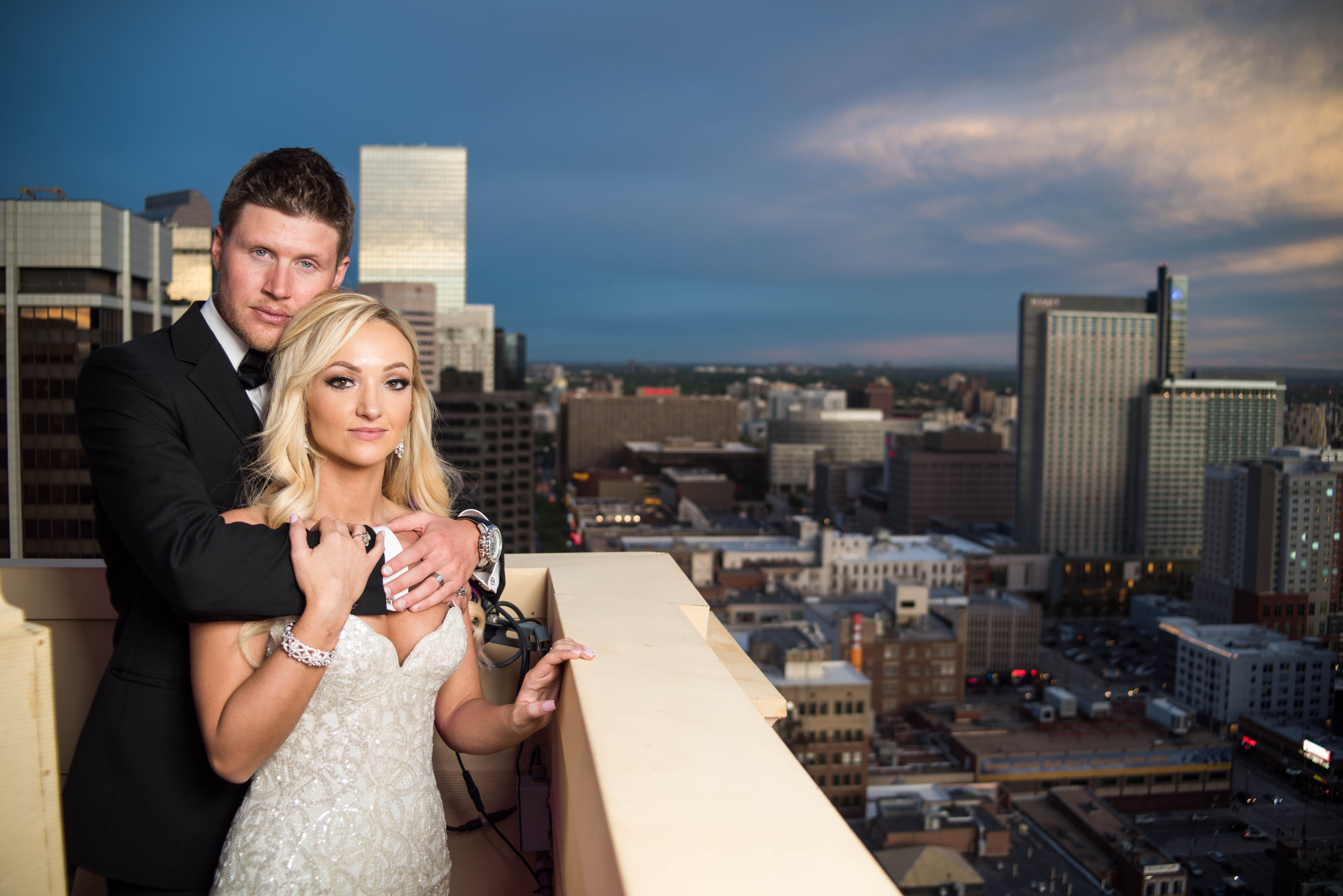 Bride and groom posing on a city rooftop at twilight with a skyline background.