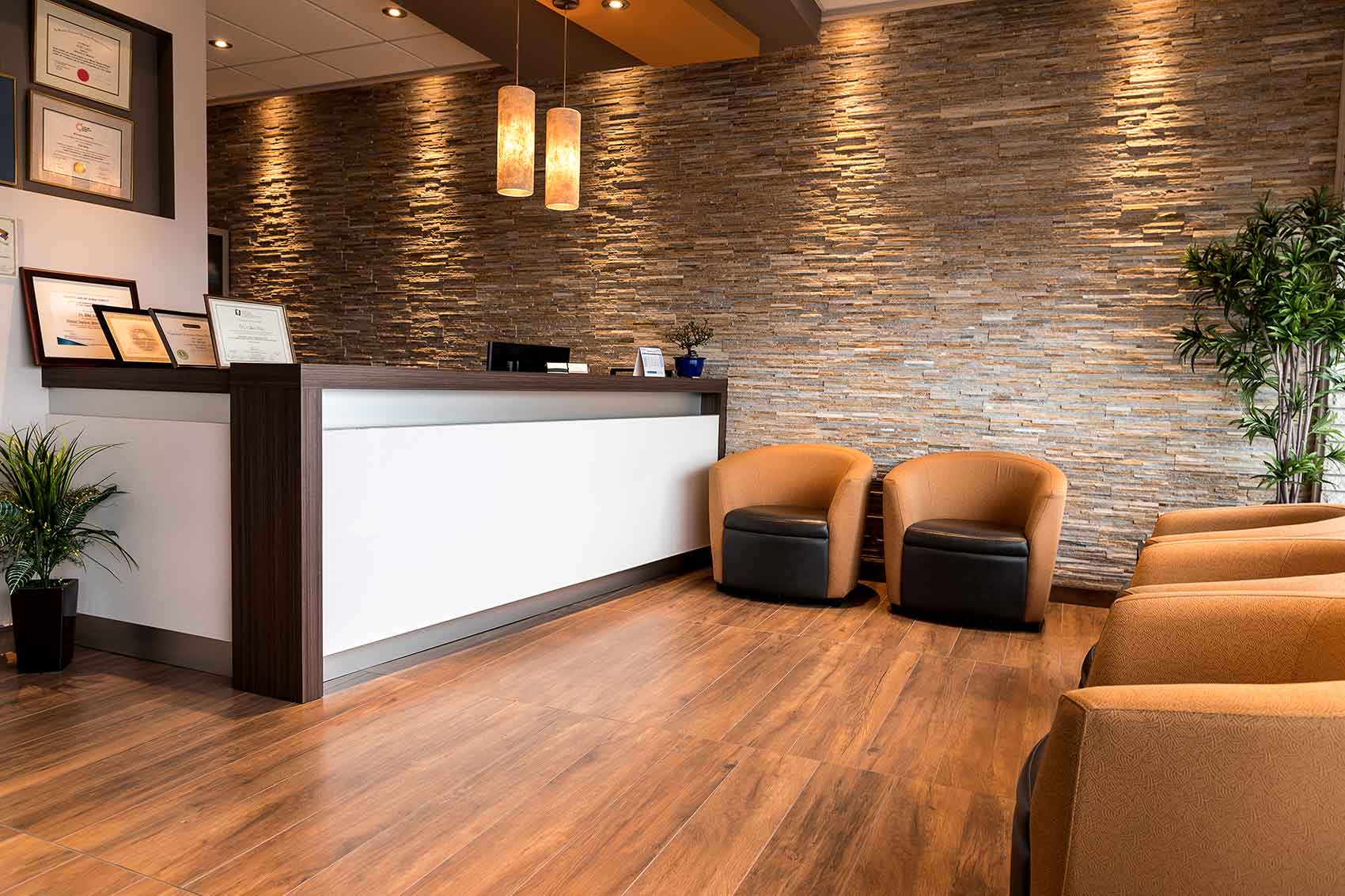 Modern dental clinic waiting and reception area with a stone feature wall and chairs.