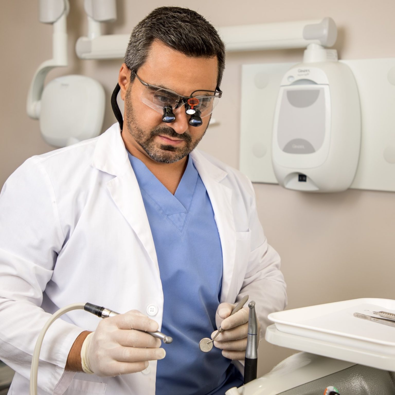 Dentist wearing loupes and holding dental tools in a clinic.