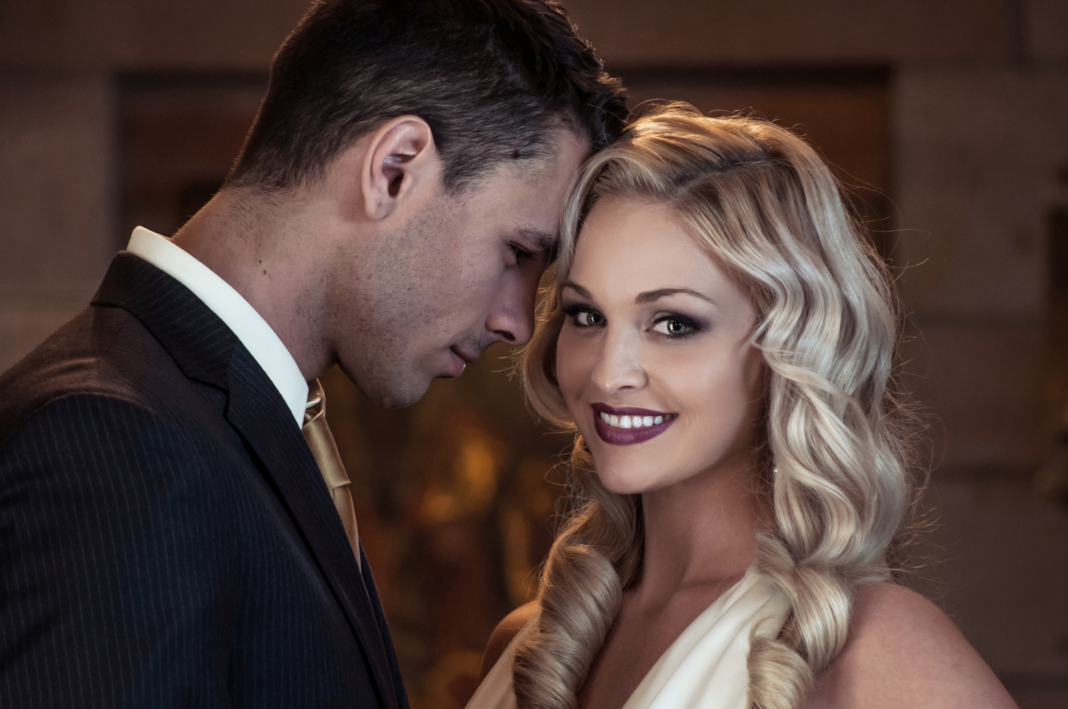 Close-up portrait of a smiling blonde bride and a groom in a dark suit.