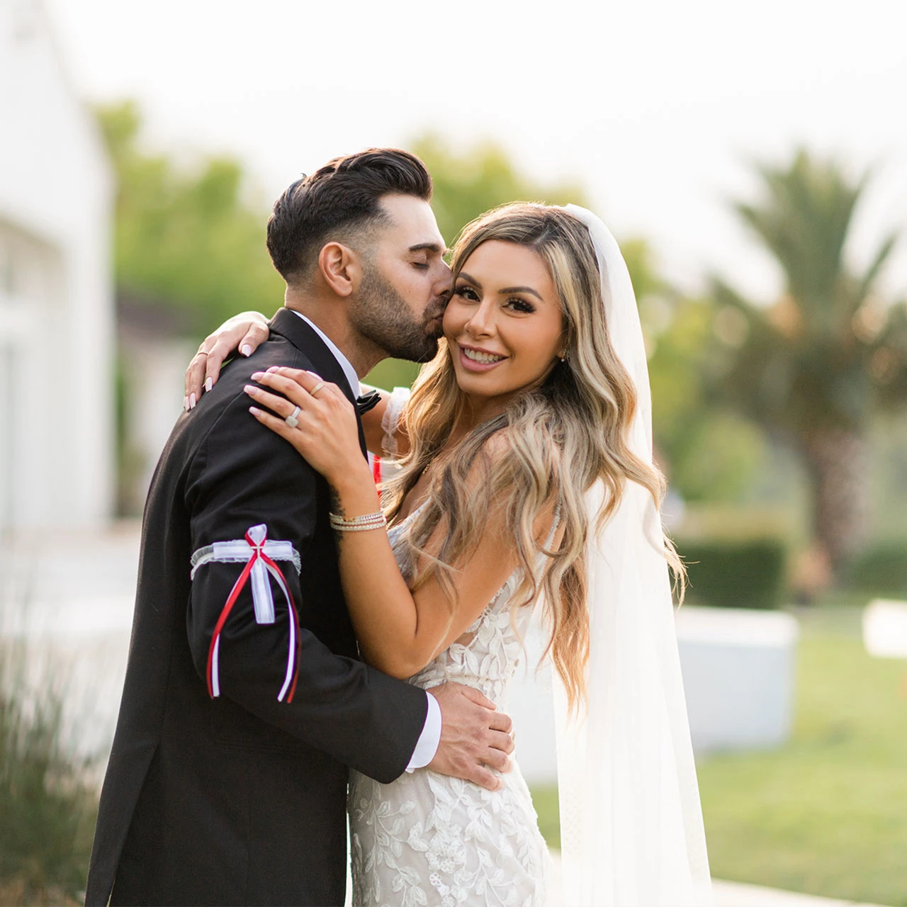 Groom kissing smiling bride on the cheek outdoors on their wedding day.