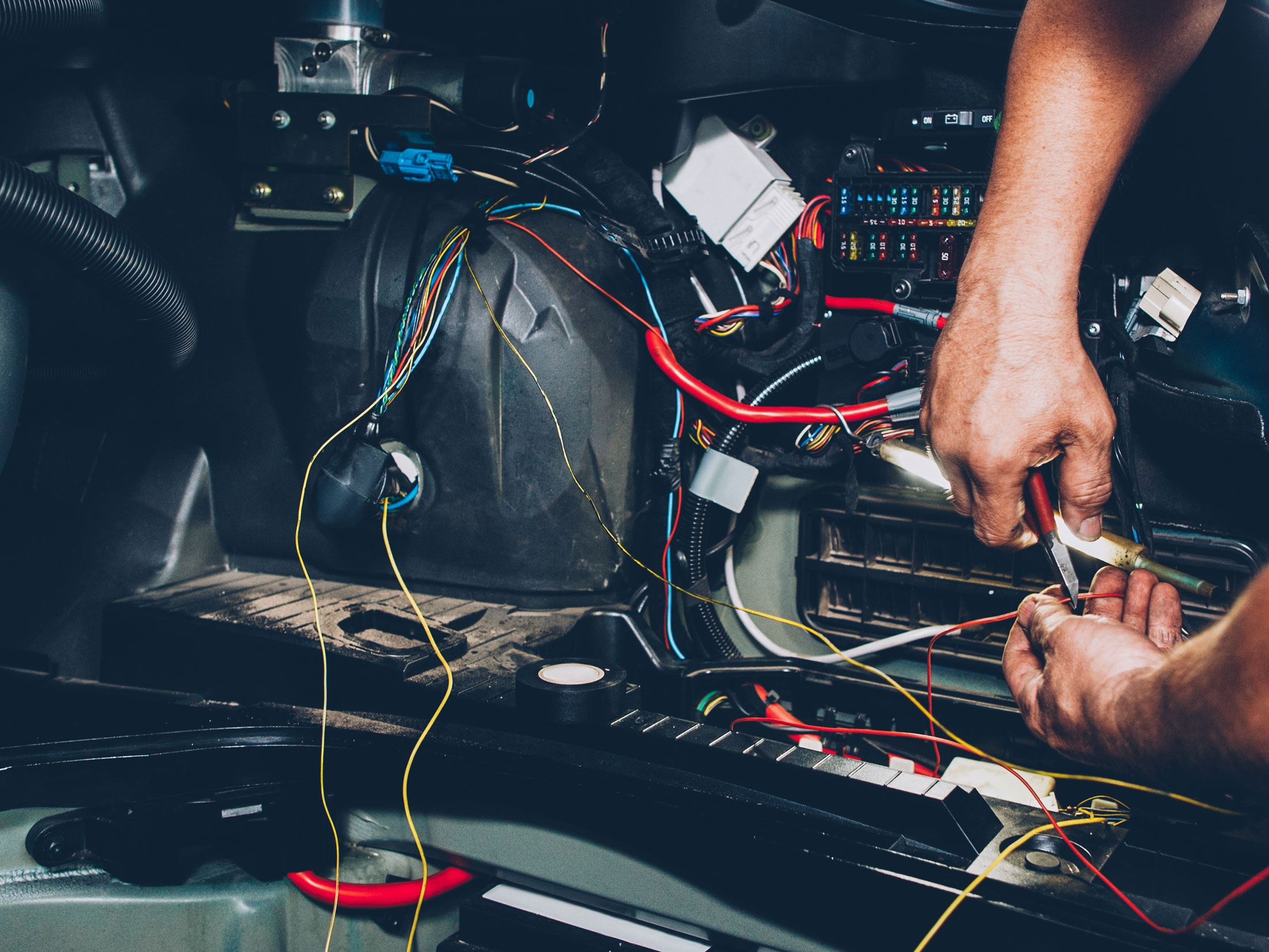 Mechanic working on automotive electrical wiring inside a car.