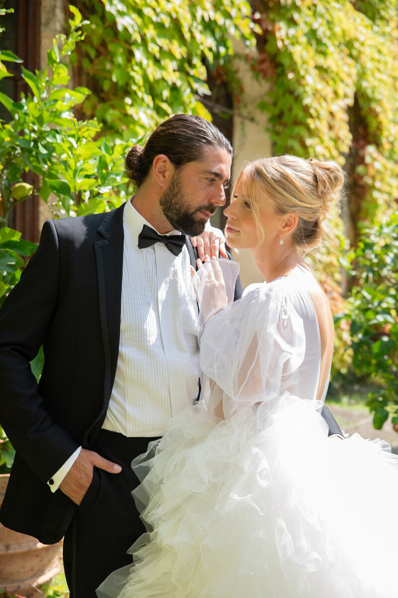 Bride and groom in formal attire posing outdoors near an ivy-covered wall.