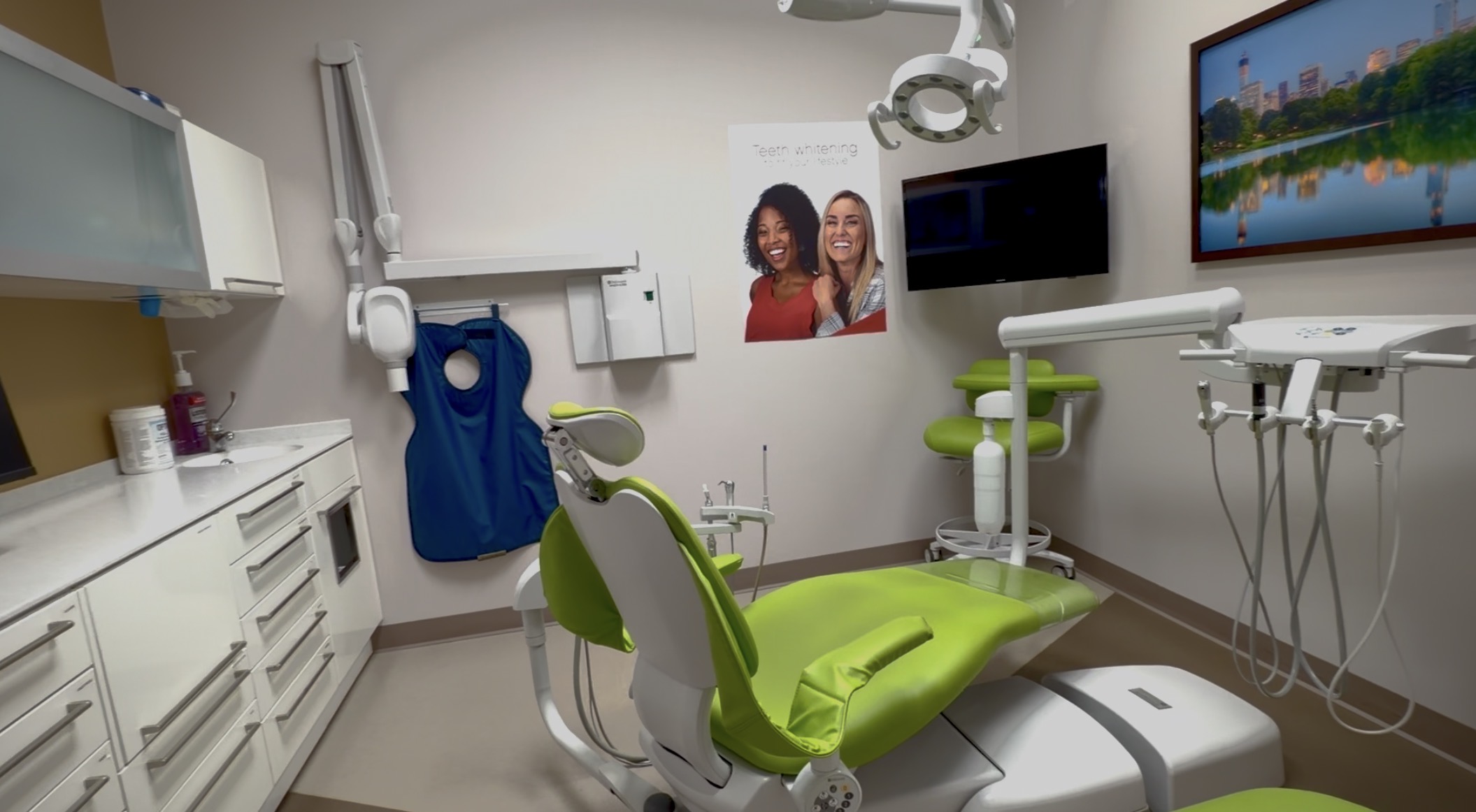 Modern dental examination room with a green treatment chair and medical equipment.