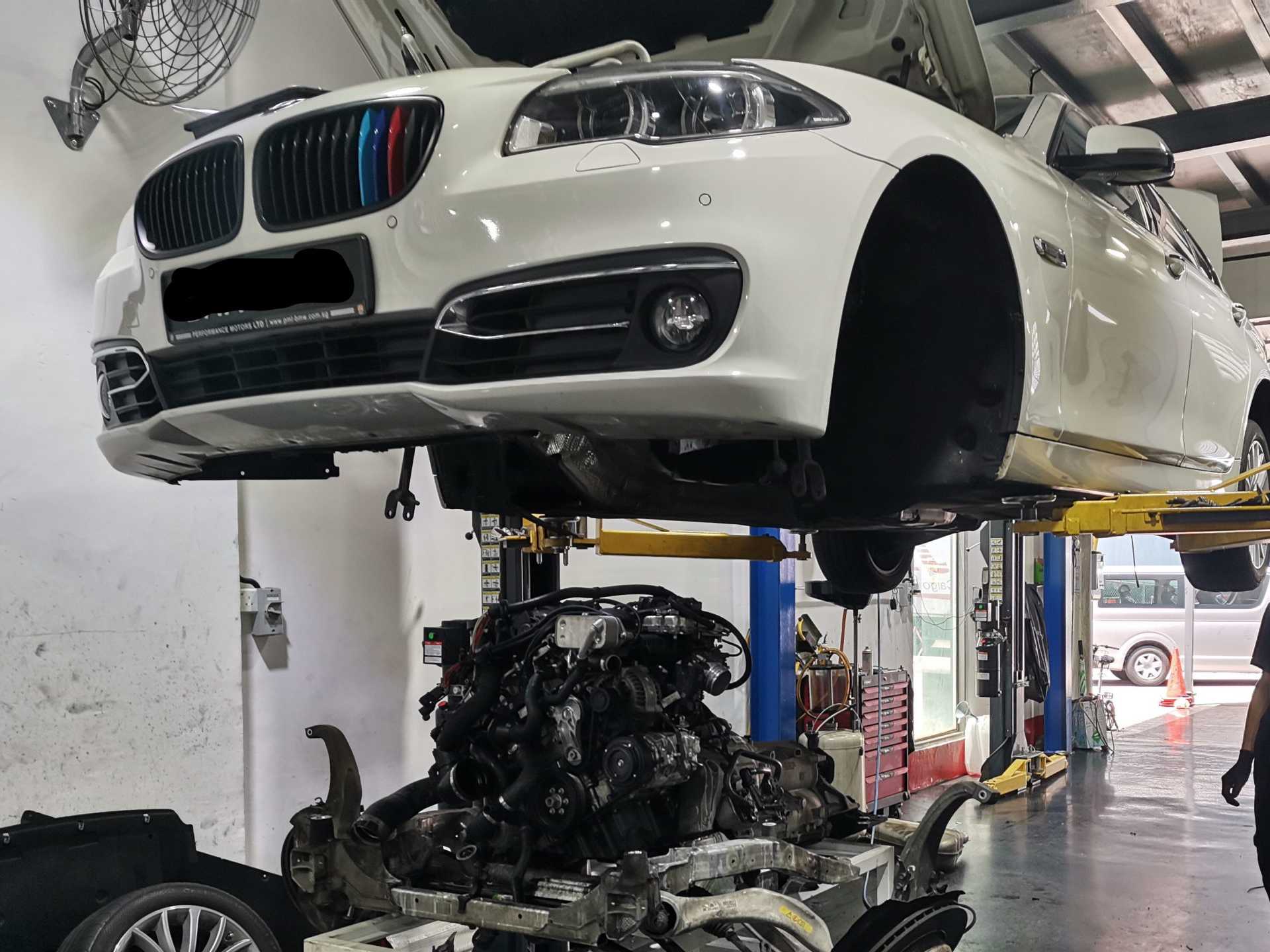 White BMW on a lift with its engine removed in a repair shop
