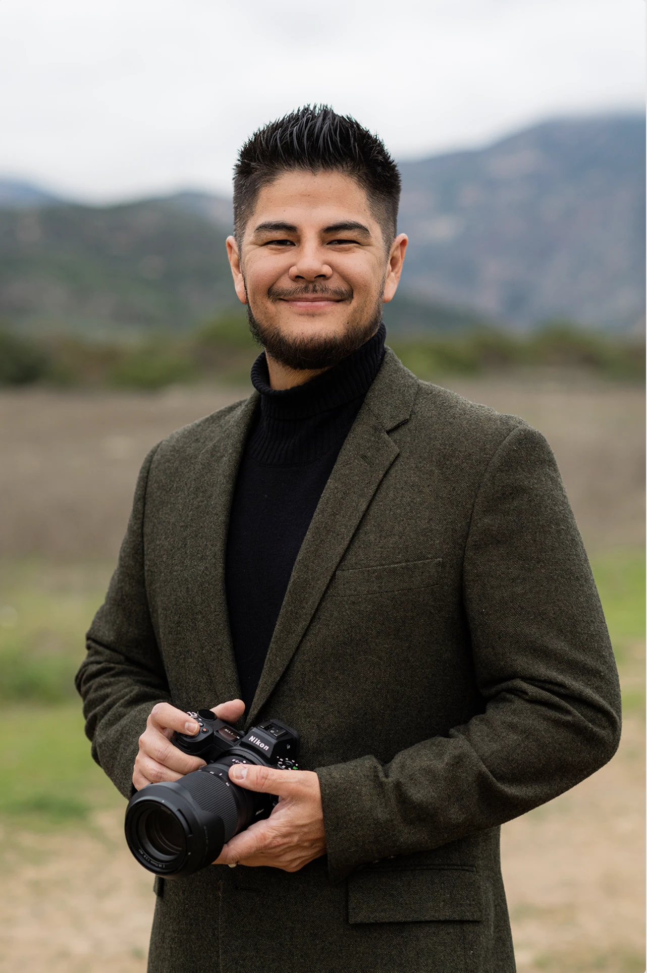 Portrait of Andrew, lead photographer for Amori Weddings, holding a camera outdoors.