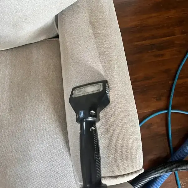 Upholstery cleaning tool cleaning the armrest of a fabric couch.