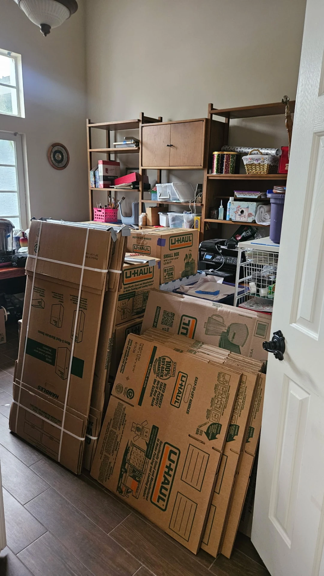 Flat-packed cardboard moving boxes stacked in a room during a downsizing preparation.