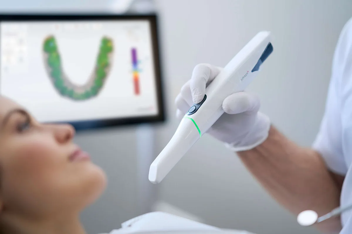 Dentist holding a digital intraoral scanner near a patient in a clinic.