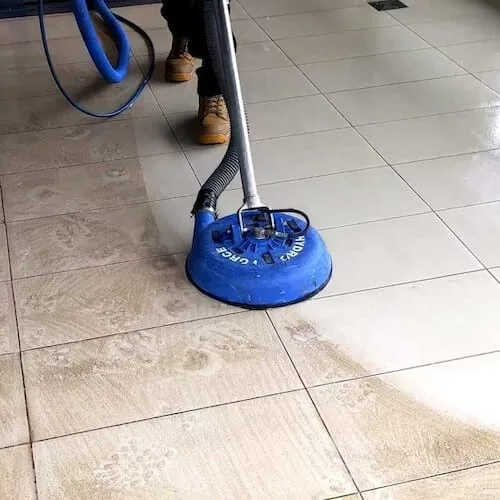 Technician cleaning dirty tile and grout with a round blue machine.