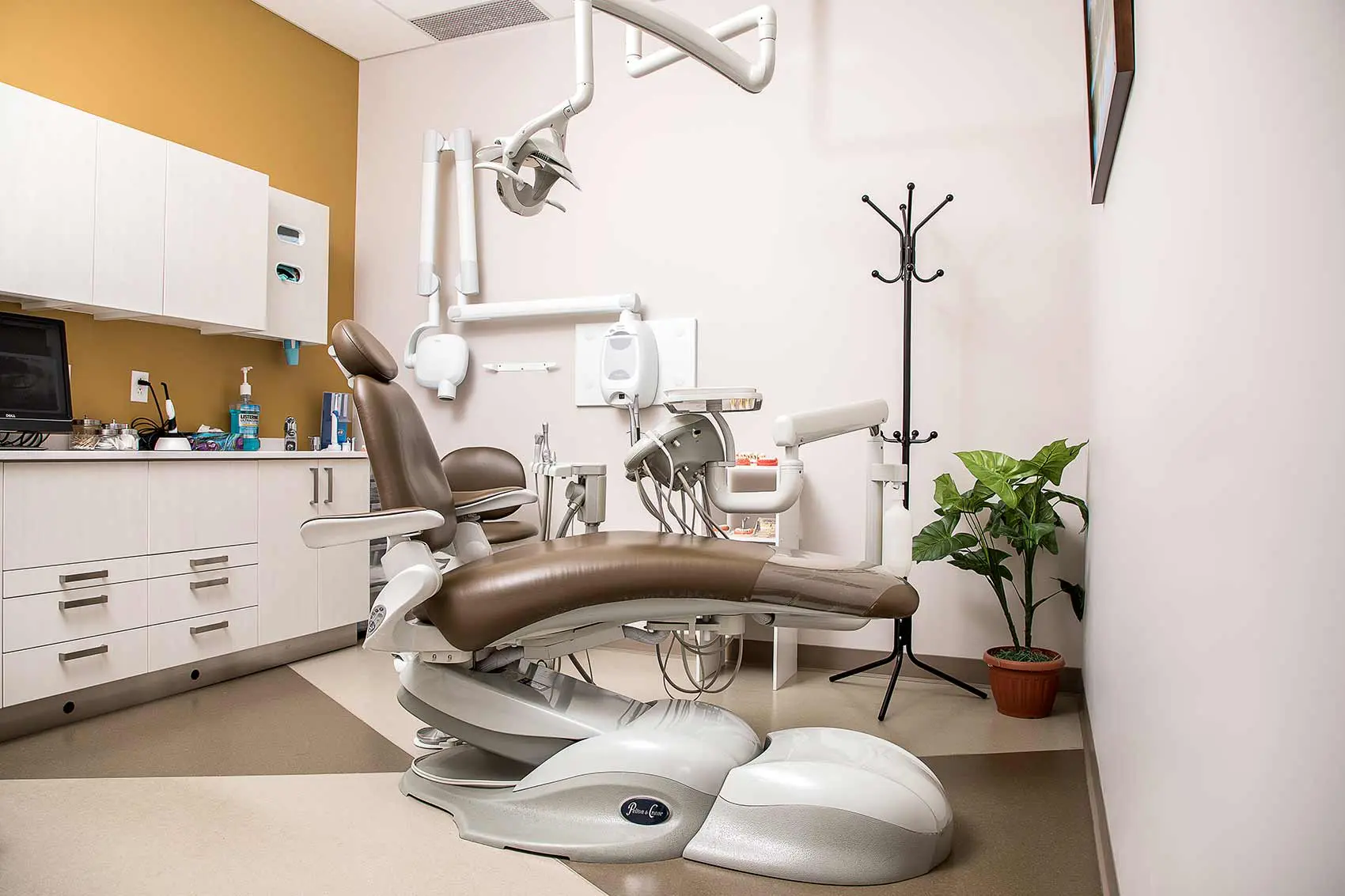 Interior view of a modern dental examination room with a brown chair and medical equipment.